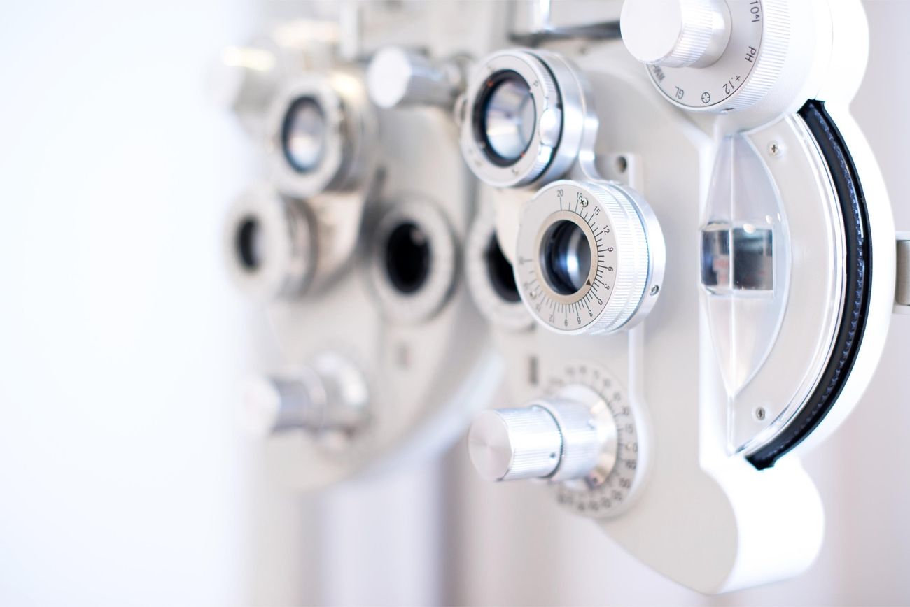Nahaufnahme eines Phoropters für die Augenuntersuchung mit silbernen Zifferblättern und Linsen vor einem unscharfen weißen Hintergrund, der auf eine optometrische Einstellung hinweist.